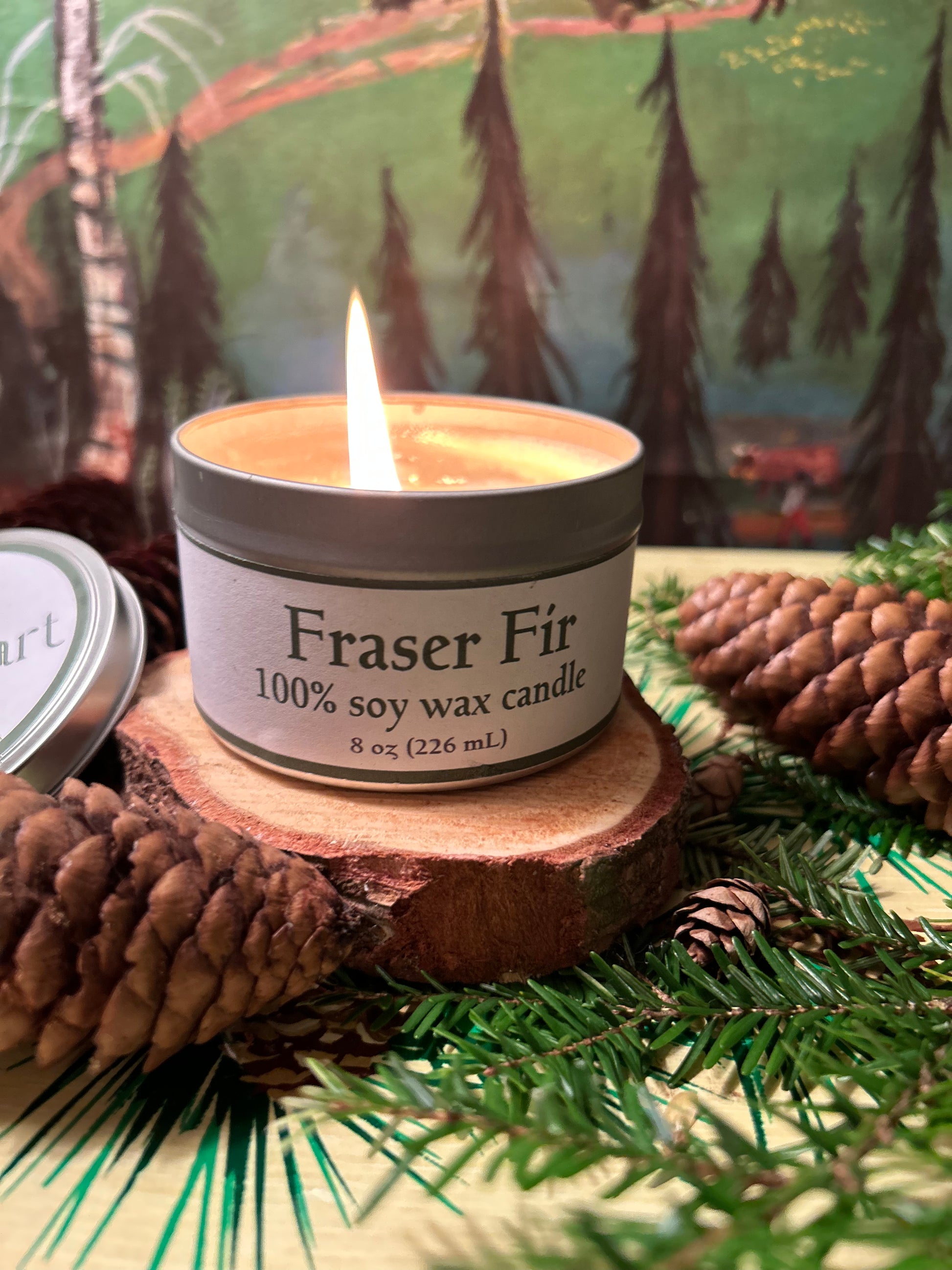 A burning Fraser Fir soy wax candle sitting on a piece of wood.