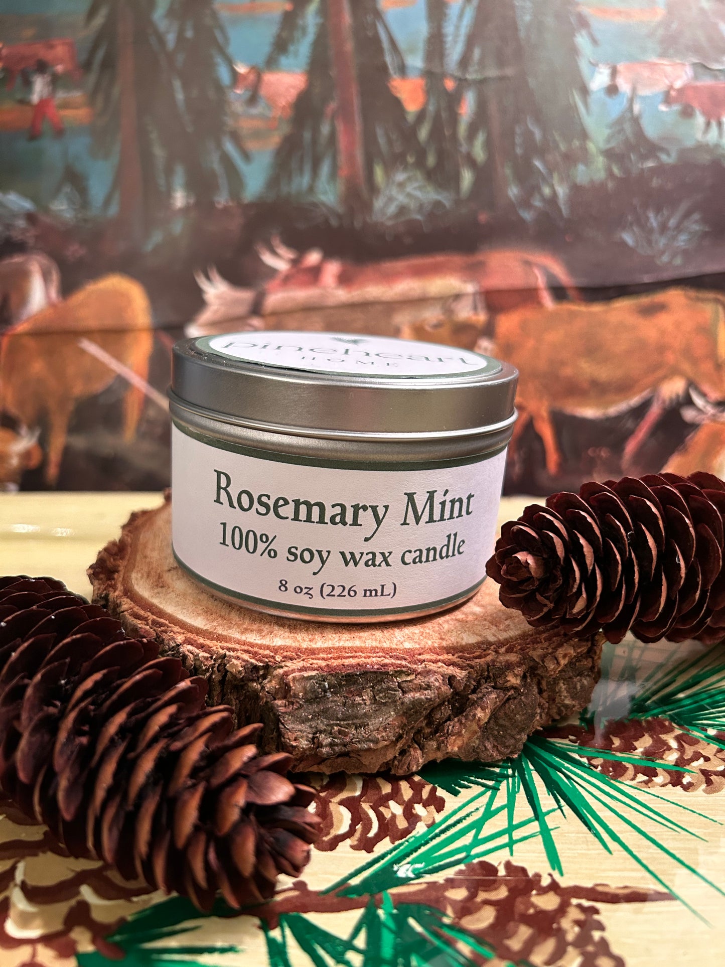 Rosemary Mint soy wax candle in an 8 oz. tin sitting on a piece of wood with pinecones.