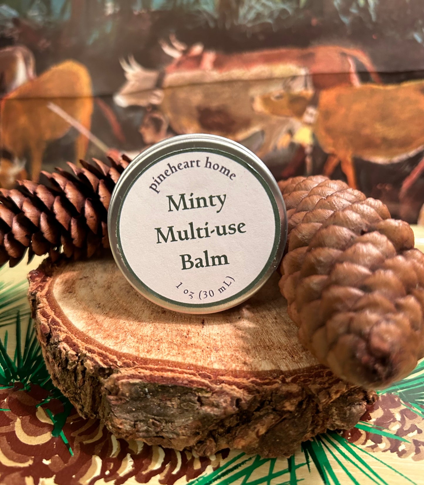 Small Minty Multi-use balm in a 1 oz. small tin, sitting on a piece of wood with pinecones.